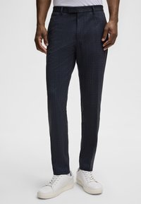 Navyblaue gemusterte Hose mit strukturiertem Finish, geradem Schnitt, seitlichen Taschen und einem Bund mit Gürtelschlaufen, kombiniert mit weißen Sneakers.