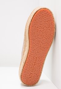 Grå sko med texturerad orange gummisula och naturlig jute-detalj längs kanten, som visar en rundad form och mjuk yta.