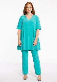 Turquoise tuniek met korte mouwen en V-hals, gecombineerd met bijpassende broeken. Zachte, soepelvallende stof met een ontspannen pasvorm en een gladde textuur.