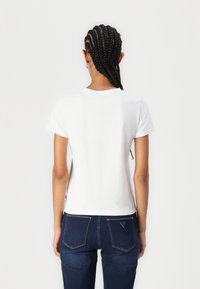T-shirt en coton blanc à manches courtes, col rond, texture lisse et silhouette ajustée, associé à un jean bleu foncé avec poches arrière.