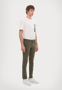 Fehér, rövid ujjú póló zöld folttal, olíva zöld, slim-fit nadrág és fehér sportcipő. Egyszerű dizájn, minta vagy kiegészítők nélkül.