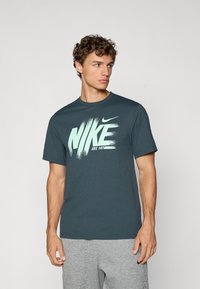 Marineblå bomulds t-shirt med korte ærmer, prydet med et stort hvidt penselstræk-agtigt "NIKE" logo og "EST. 1971" i lys mintgrøn skrift.