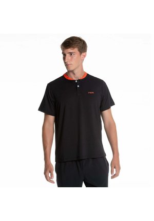 Giovane uomo che indossa una maglia henley nera a maniche corte con due bottoni e un piccolo logo rosso sul petto, che guarda leggermente verso sinistra.