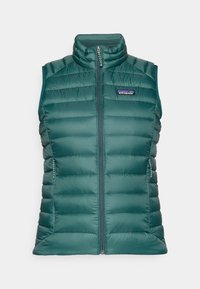 Zeleni prsluk s pjenastim punjenjem, visokim ovratnikom i prednjim zatvaračem na zip. Ima bočne džepove i šavnu obradu za izolaciju. Patagonia logotip na prednjoj strani.