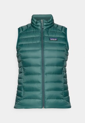 Chaleco acolchado verde con cuello alto y cierre frontal de cremallera. Cuenta con bolsillos laterales y detalles cosidos para aislamiento. Logo de Patagonia en la parte delantera.