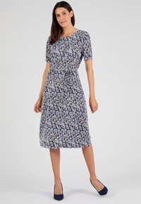 Vestido floral en tonos azules, blancos y amarillos. Manga corta, escote redondo, cintura elástica y falda a la altura de la rodilla. Tacones de ante azules.