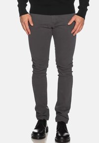 Pantaloni slim-fit grigio scuro realizzati in tessuto elastico, con una superficie liscia e gambe affusolate, abbinati a scarpe nere.