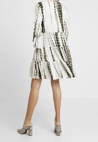 Klänning i vitt med gröna tie-dye-mönster, med lagerdesign, långa ärmar och rund halsringning. Kombinerad med texturerade klackar i ormskinnsmönster.