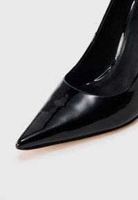 Mustast lakknahast kõrge kontsaga king, millel on terav nina ja sile pind; sisu on musta värvi, kergelt läikiv.