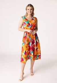 Kleid mit V-Ausschnitt und ohne Ärmel in leuchtendem Orange, Gelb und rosa Blumenmustern auf einem weißen Hintergrund; hat einen elastischen Taillenbund und einen flatternden Rock.