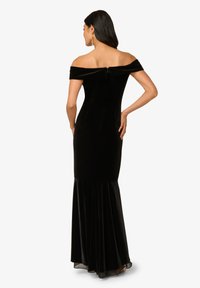 Zwarte fluwelen off-shoulder jurk met een getailleerde body en een uitlopende rok. Heeft een rits aan de achterkant en een satijnen textuur.