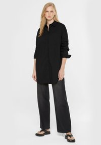 Black long-sleeve shirt with a collar and front pocket, made of smooth fabric. Paired with black wide-leg jeans and flat sandals.