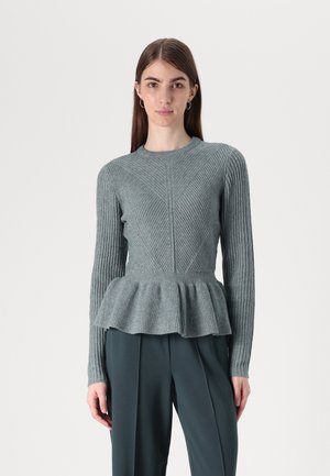 Pull en maille gris clair avec une texture côtelée, taille peplum et manches longues présentant des motifs en chevron. Assorti avec un pantalon vert foncé.