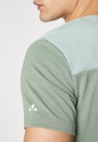 Camicia a maniche corte nei colori verde chiaro e menta, con una texture morbida e un piccolo logo bianco sulla manica. Cucitura della spalla allungata.