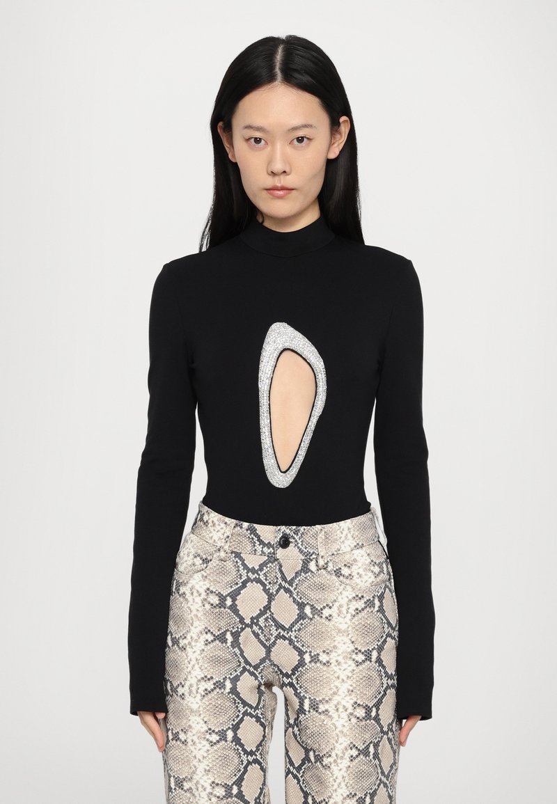 Black long-sleeve bodysuit with a cutout outlined in rhinestones, paired with light-colored snake-print pants featuring a fitted design.