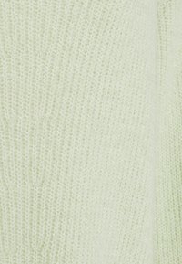 Gros plan d’un tissu tricoté doux vert clair montrant une fine texture du fil duveteux avec de petits motifs de points réguliers.