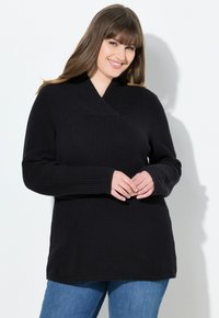 Maglione nero a maglia con scollo a V profondo, maniche lunghe e texture a coste. Abbinato a jeans blu, che mostrano una vestibilità comoda.