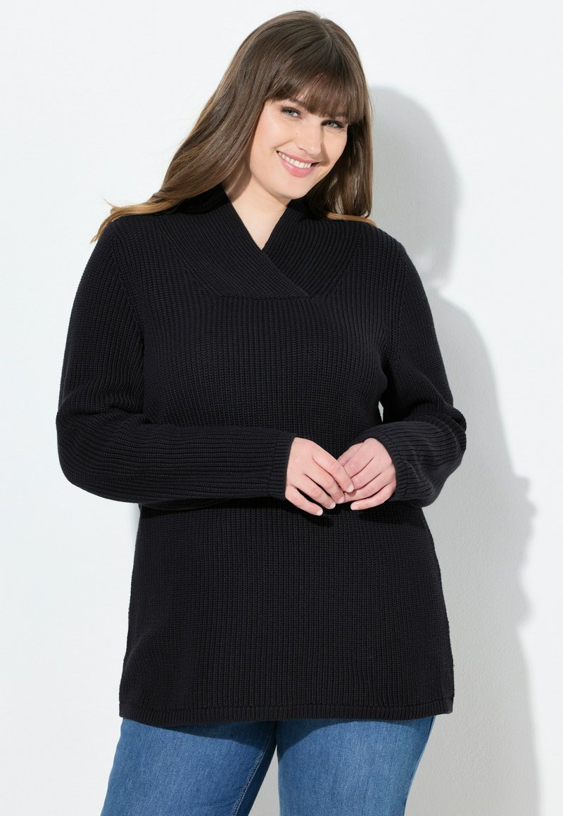 Maglione nero a maglia con scollo a V profondo, maniche lunghe e texture a coste. Abbinato a jeans blu, che mostrano una vestibilità comoda.