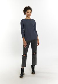 Tricou lung cu mânecă din tricot de culoare bleumarin, cu un finisaj texturat, asortat cu blugi negri deteriorați și cizme negre cu șireturi. Siluetă casual, ajustată.