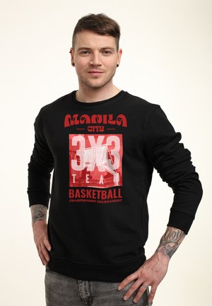 Mand med øreringe og tatoveringer iført sort sweatshirt med rød og hvid tekst "Manila City 3x3 Basketball Championship Tournament" og grafik af en basketballkurv.