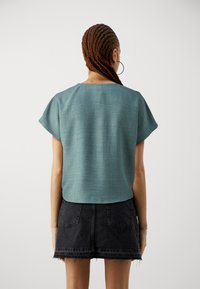 Tyrkis kortermet topp med en teksturert finish, kombinert med et høyt liv sortdenims skjørt med frynset kant og baklommer.