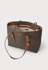 Sac fourre-tout en toile marron avec un motif de logo discret, des accents en cuir beige, des doubles poignées et une poche intérieure zippée.
