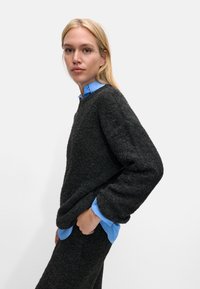 Ciemnoszary sweter o fakturze z luźnym krojem, zestawiony z jasnoniebieską koszulą z kołnierzykiem. Sweter ma opadające ramiona i szerokie rękawy.