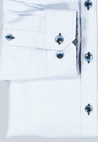 Himmelblaues Hemd mit langem Arm und Manschette, dunklen Knöpfen und subtilem geometrischem Muster, wobei die Manschette ordentlich gefaltet ist.