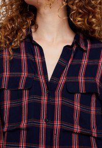 Navy plaid button-up shirt featuring red and white stripes, two chest pockets, and a V-neck design with a soft texture.