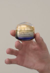 Shiseido Vital Perfection ögonkräm i en rund behållare med ett guldlock och blå botten, med metallisk text på framsidan.