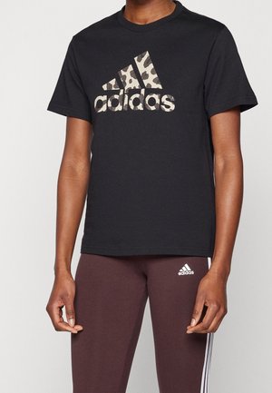 Henkilö, jolla on musta Adidas-t-paita, jossa on leopardikuvioinen logo, ja tummanruskeat Adidas-legginssit valkoisilla raidoilla sivuilla.