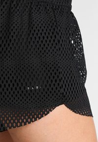 Pantalones cortos de tela negra perforada con una cintura elástica, con un dobladillo festoneado y un diseño de malla texturizada. Transpirables y ligeros.