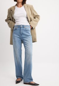 Vaaleansiniset korkeavyötäröiset farkut, joissa on klassinen viiden taskun muotoilu. Yhdistetty beigenväriseen oversized-takkiin ja mustiin litteisiin kenkiin.