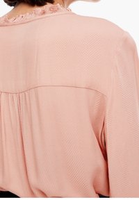 Blouse rose avec un motif chevron texturé, un col volanté et une coupe ample avec des fronces dans le dos.