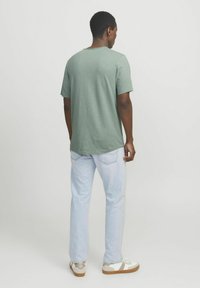 Green cotton crew-neck t-shirt with short sleeves, relaxed fit. Paired with light blue denim jeans and white sneakers with brown accents.