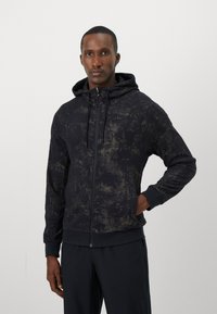 Sudadera negra con un patrón texturizado, cierre con cremallera en la parte delantera y capucha. Presenta un corte holgado y acentos oscuros contrastantes en los puños y el dobladillo.