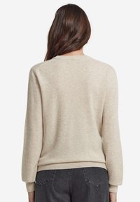 Beige stickad tröja med mjuk textur, rund halsringning och ribbade muddar och nederkant. Baksidan har en enkel design utan några dekorationer.