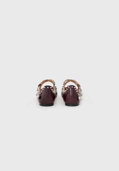 Zapatos de cuero burdeos con abertura en la parte trasera, decorados con tachuelas plateadas y herrajes decorativos en el tacón. Suela plana, diseño minimalista.