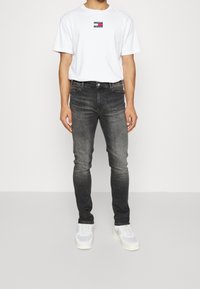 Camiseta blanca con un pequeño logo multicolor, jeans oscuros ajustados de color gris, y zapatillas gris claro. Diseño simple, material de algodón, corte slim.