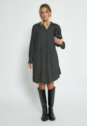 Black, long-sleeve dress with white dot pattern, collar, and button-down front. Paired with knee-high black boots and a black clutch purse.