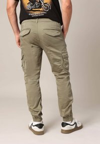 Groene cargobroek gemaakt van lichtgewicht stof, met zijzakken, elastische boorden en een zachte textuur. Draag met witte sneakers.