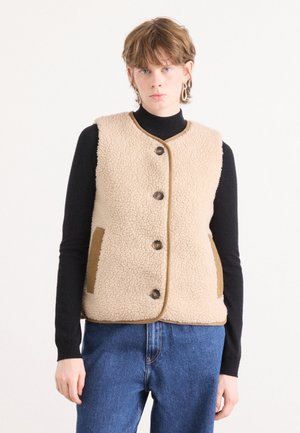 Beige fleece vest met een ronde hals, vijf donkere knopen en bruine zijzakken. Gecombineerd met een zwart longsleeve shirt en denim broek.