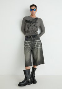 Grijze lange mouwen shirt met zwart grafisch ontwerp, brede zwarte denim shorts met vervaagde textuur en knie-hoge zwarte laarzen met zilveren accenten.