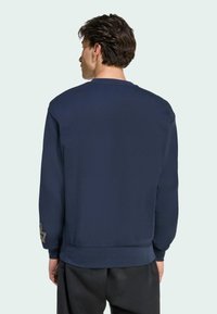 Sudadera azul marino con cuello redondo, mangas largas y puños de canalé. Presenta un logo en la manga izquierda. Textura lisa.