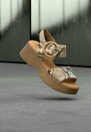Bruine plateau sandalen met een slangenhuidpatroon, voorzien van een brede band en een cirkelvormige gesp. De zool heeft een gestructureerde afwerking.