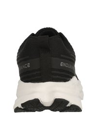 Svart träningsskor med en texturerad ovandel, utrustad med en dragrem, vit dämpande sula och en svart gummisula med mönster för grepp.