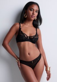 Soutien-gorge en dentelle noire et string assorti avec des motifs géométriques intriqués, une touche d'or sur le soutien-gorge et des bretelles réglables. Texture lisse.