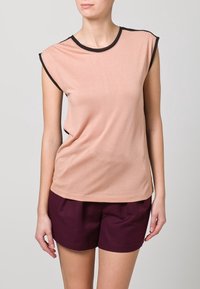 Peach-toned sleeveless top featuring a round neckline with black edging, soft material, and a relaxed fit, paired with dark burgundy shorts.