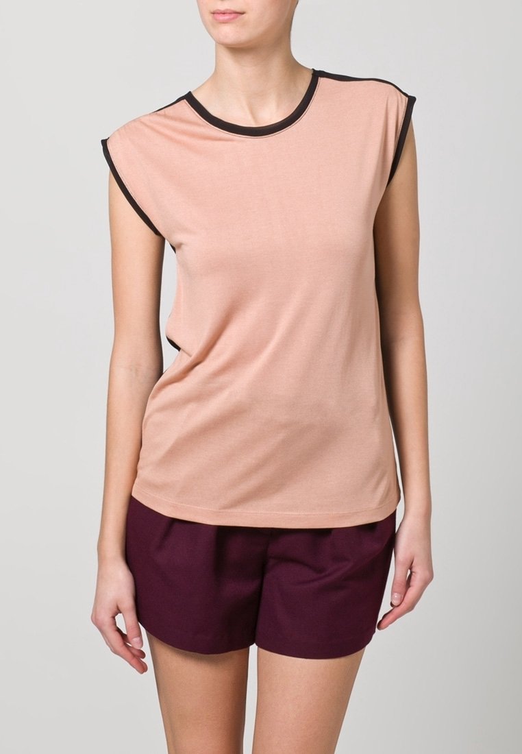 Peach-toned sleeveless top featuring a round neckline with black edging, soft material, and a relaxed fit, paired with dark burgundy shorts.