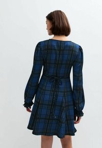 Niebieska sukienka w kratę z bufiastymi długimi rękawami, zwężoną talią i falbankowymi mankietami. Wykonana z teksturowanej tkaniny, z kontrastującymi zielonymi i żółtymi liniami.